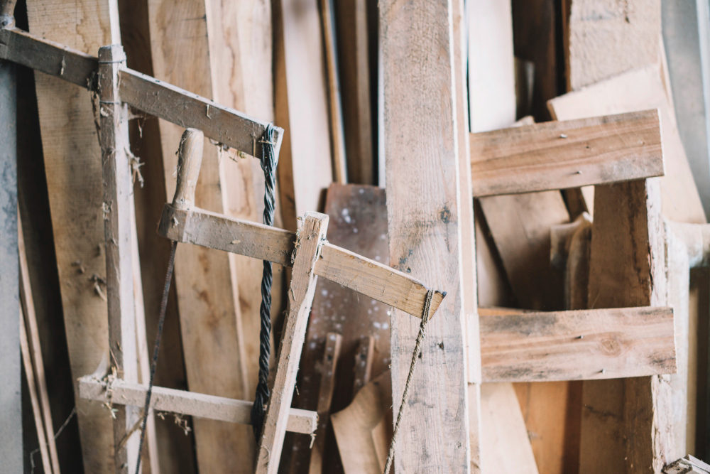 A cluttered collection of wooden planks and scraps, with a broken frame partially visible, showcasing a rustic woodworking environment.